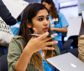 Close up on student talking in a group with a computer in front of her.